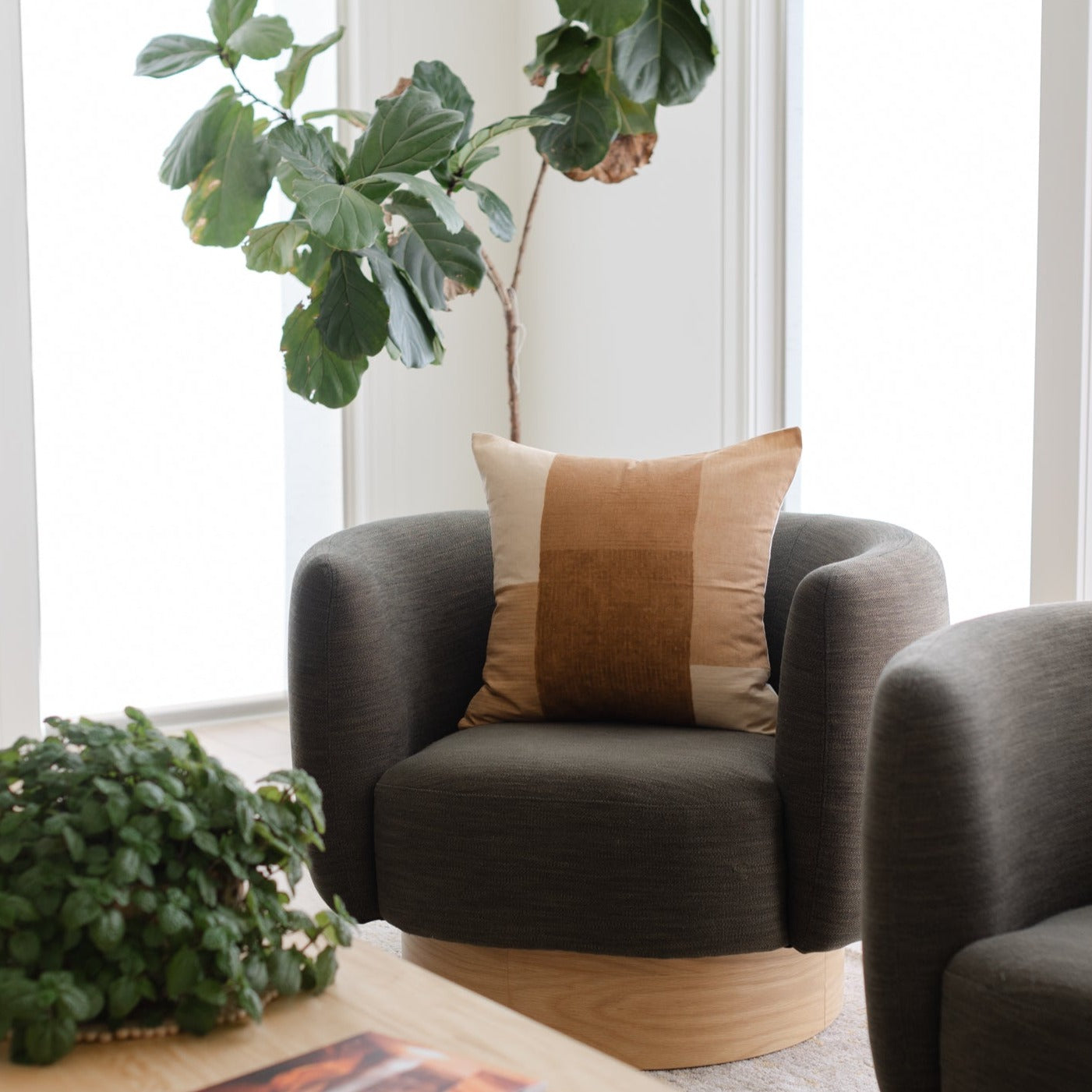 Tierra throw pillow with color-blocked design in rust, tan, and cream on dark gray chair.