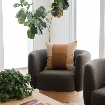 Tierra throw pillow with color-blocked design in rust, tan, and cream on dark gray chair.