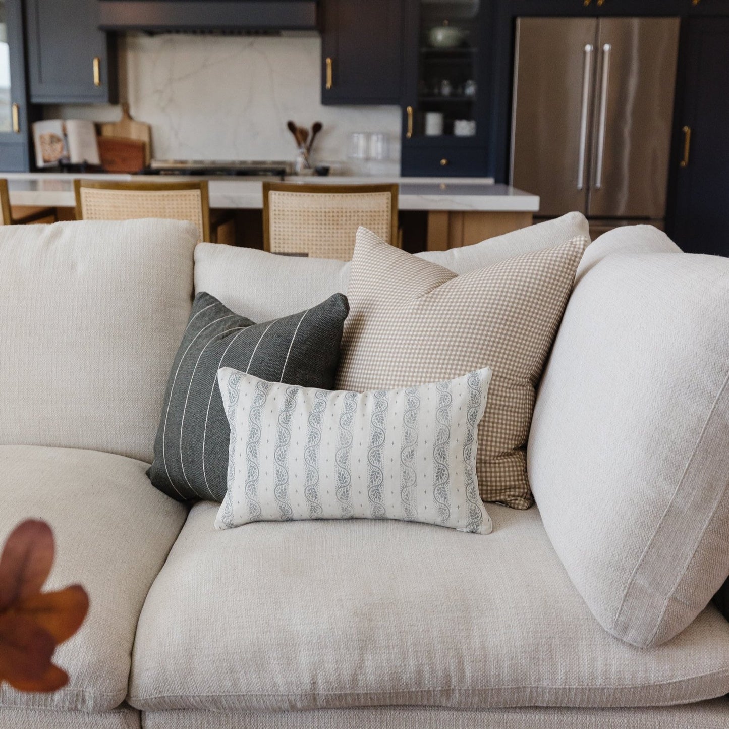 White lumbar pillow with gray paisley pattern displayed on a cream upholstered sofa with coordinating pillows.
