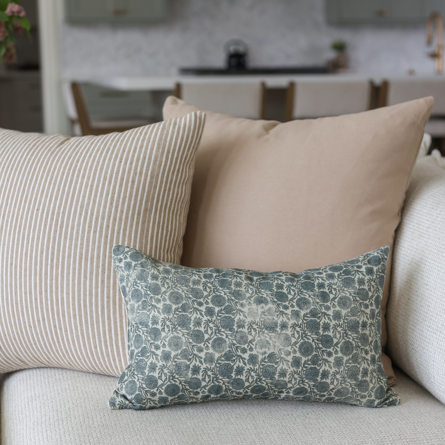 Three tan and neutral-toned pillows arranged on a light beige sofa with striped and patterned fabrics.