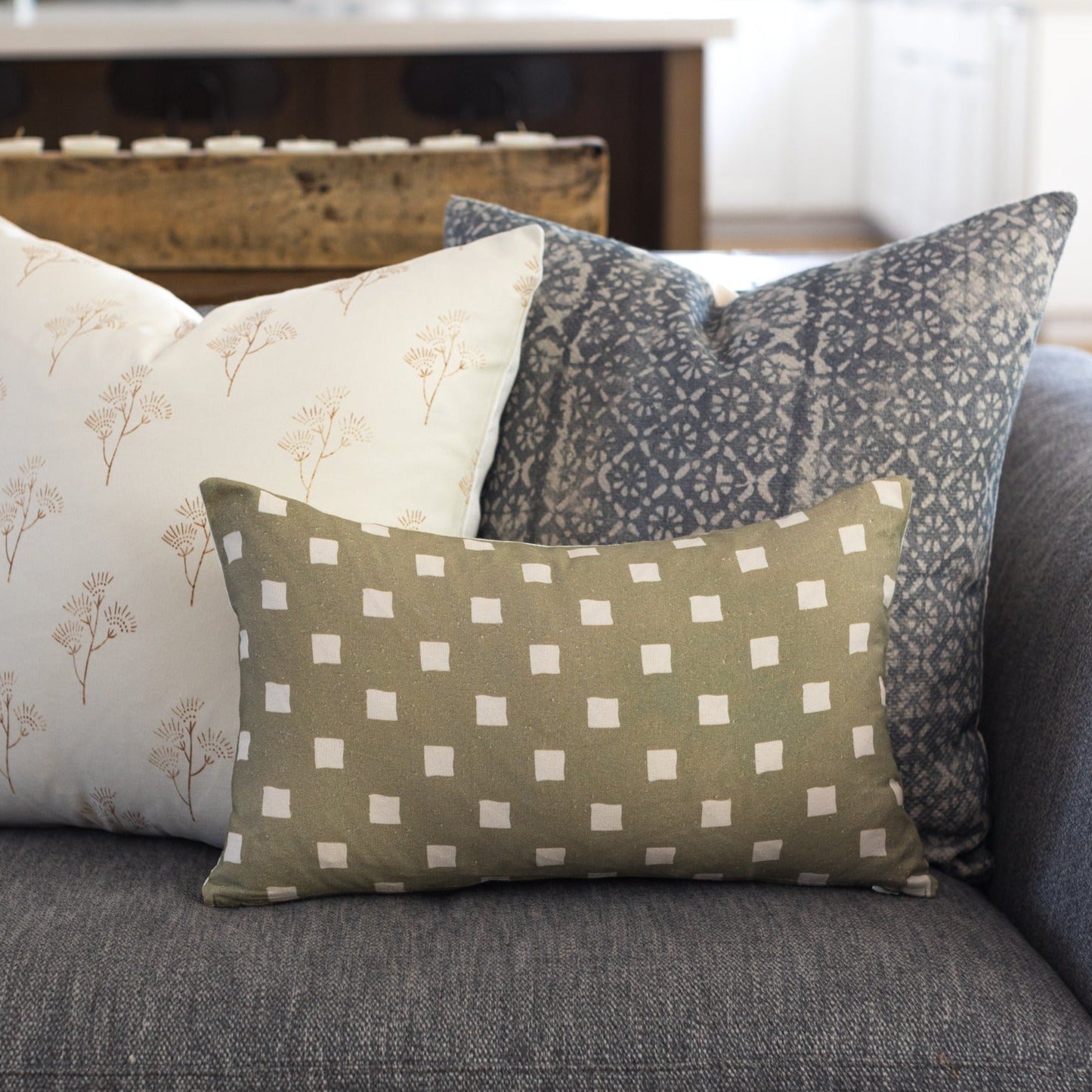 Olive-green rectangular pillow with white spaced check pattern displayed on gray sofa with coordinating pillows.