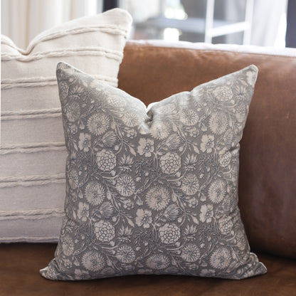 Gray and white botanical patterned throw pillow displayed on a brown leather sofa.