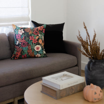 Square throw pillow with dark teal background and multicolored floral print in pink, red, orange, and white on gray sofa.