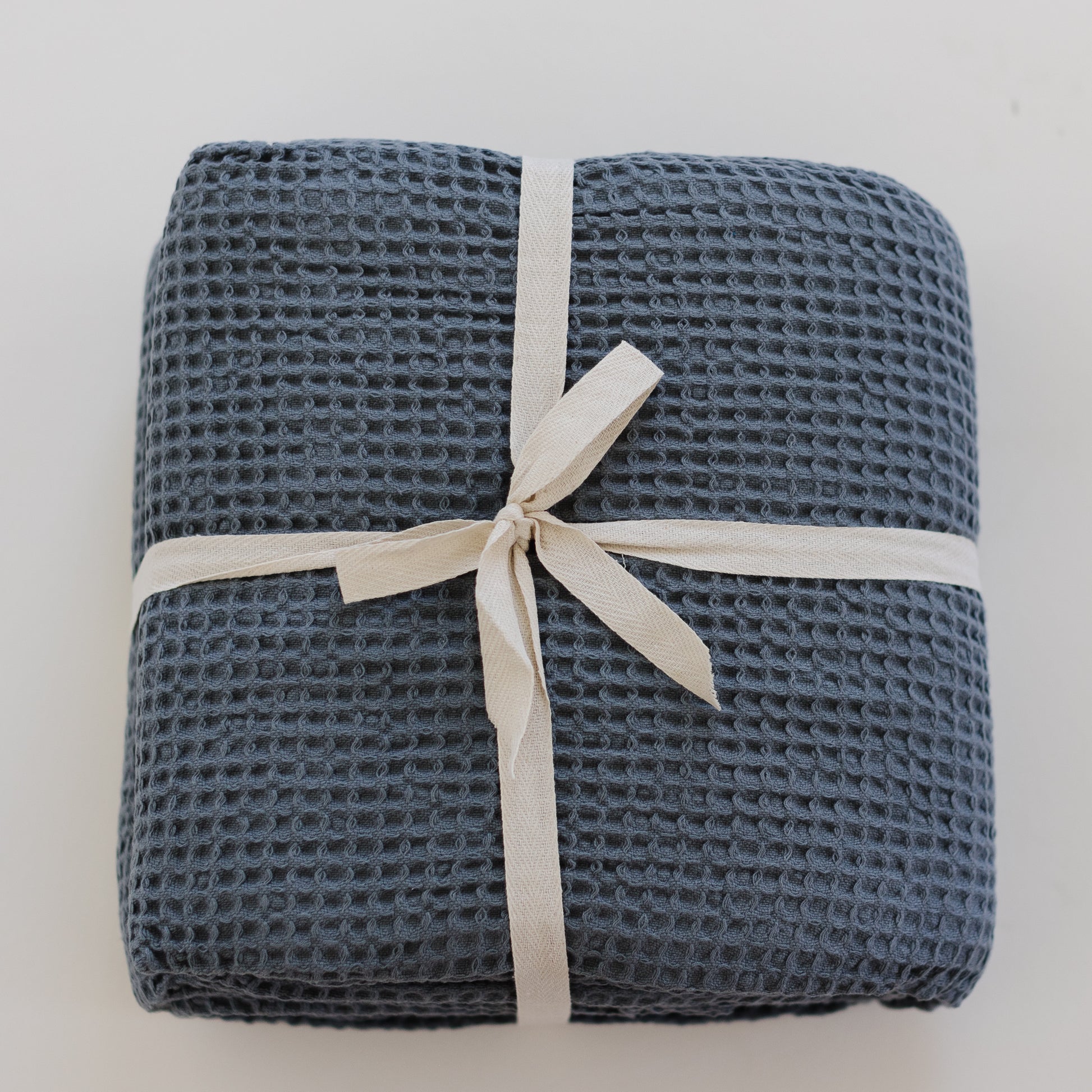 Storm blue waffle-textured blanket rolled and tied with a cream-colored ribbon bow.