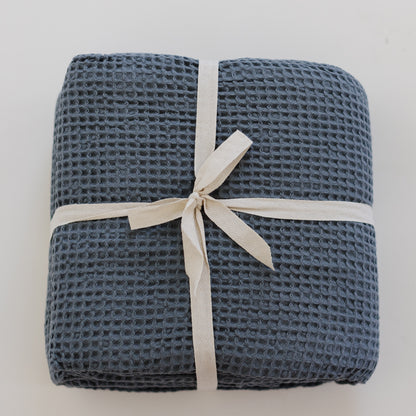 Storm blue waffle-textured blanket rolled and tied with a cream-colored ribbon bow.