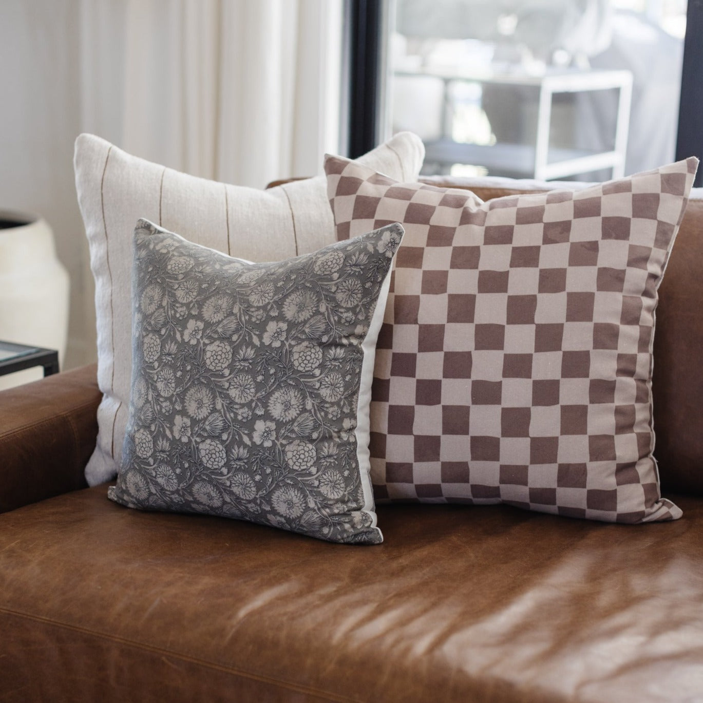 Tan and brown checkered pillow with alternating square pattern displayed on brown leather sofa.