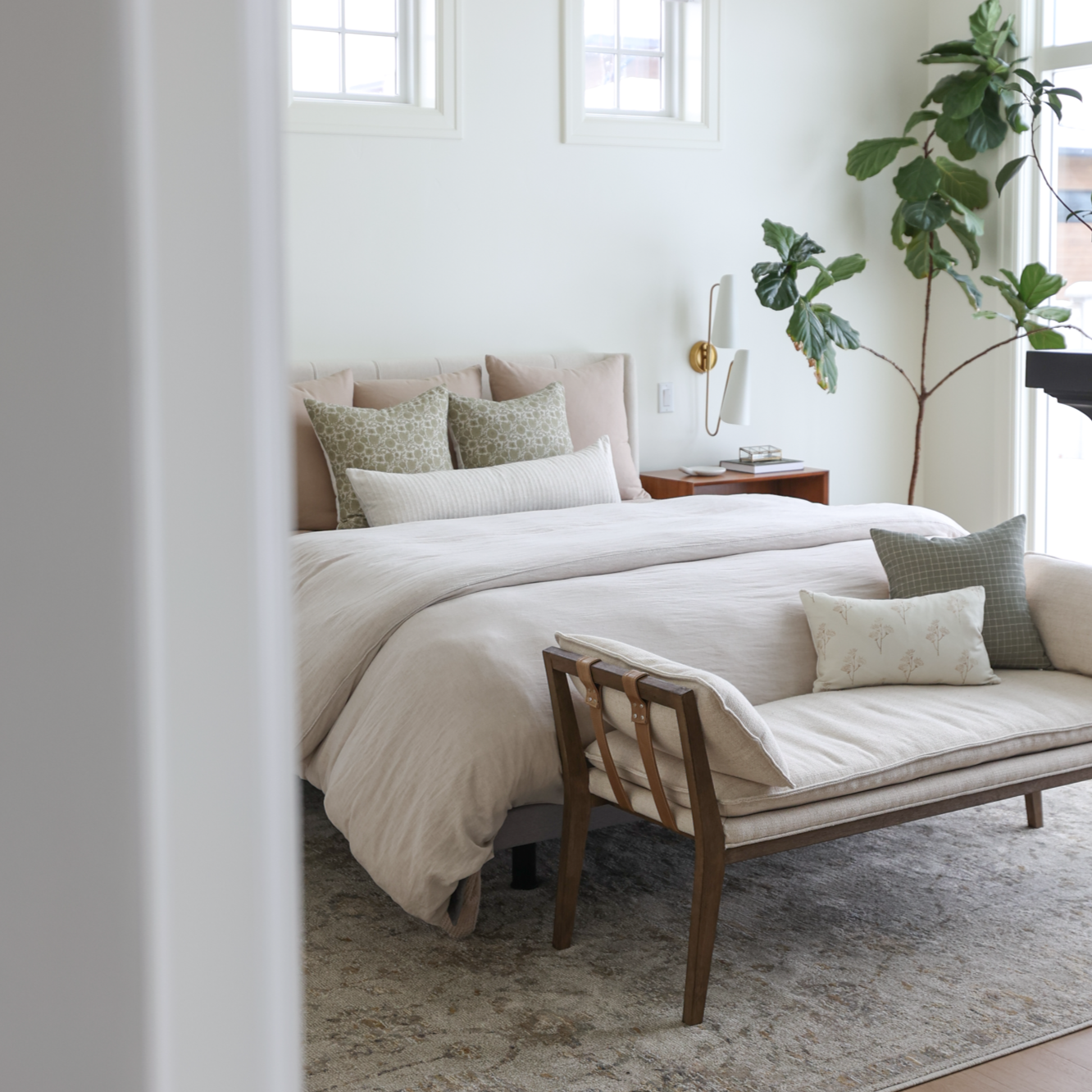 Tan and cream decorative pillows arranged on a bed with white and neutral bedding in a bedroom setting.
