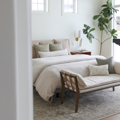 Tan and cream decorative pillows arranged on a bed with white and neutral bedding in a bedroom setting.