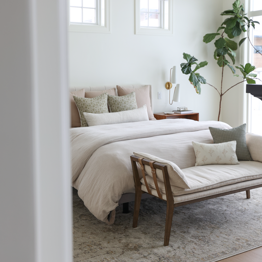 Tan and cream decorative pillows arranged on a bed with white and neutral bedding in a bedroom setting.