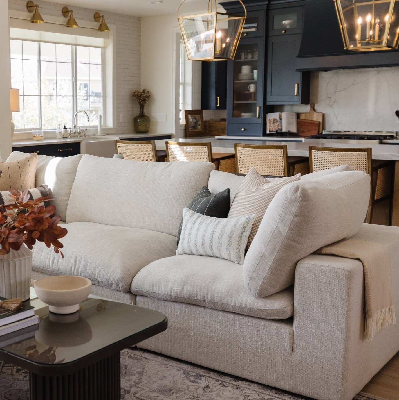 Cream lumbar pillow with vertical striping displayed on beige upholstered sofa in modern kitchen-living room setting.