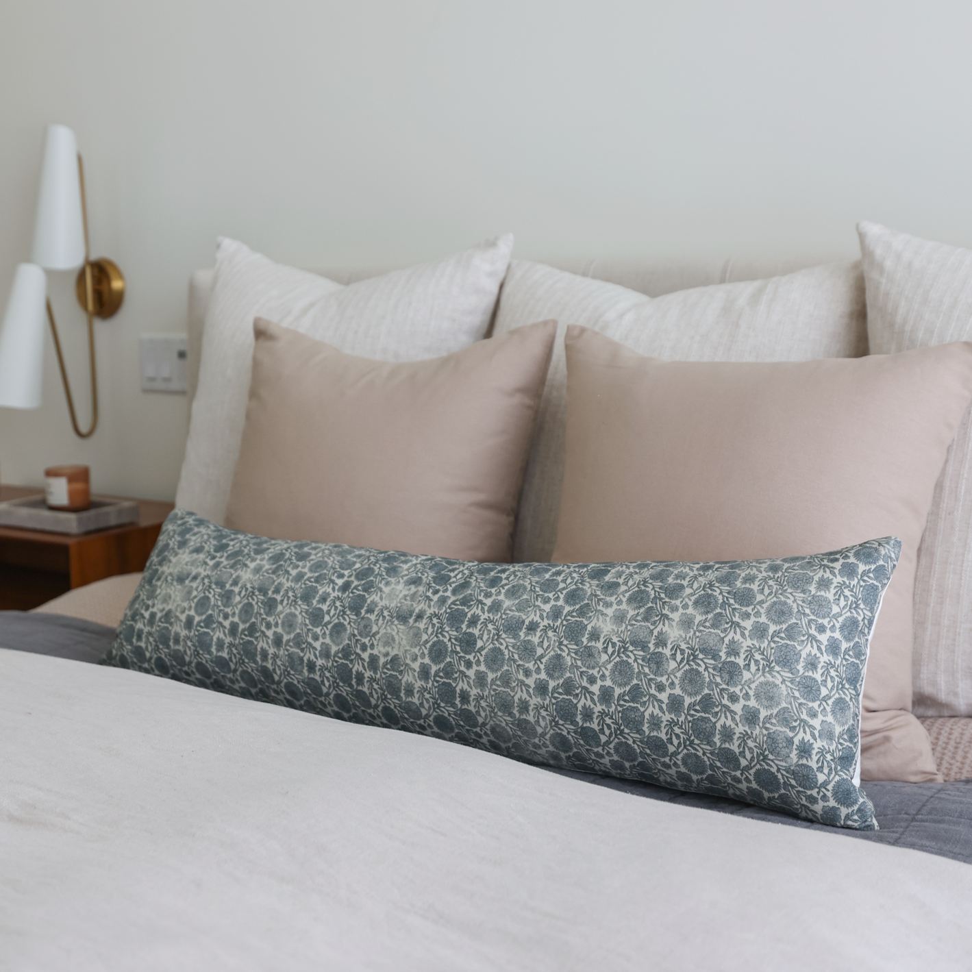Blue and white floral patterned lumbar pillow displayed on a bed with neutral pillows.