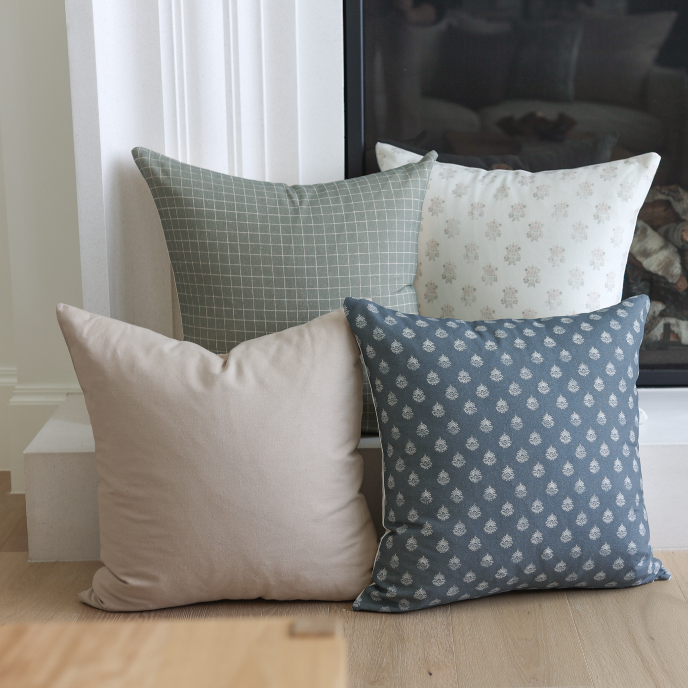 Four decorative pillows in blue, sage green, cream, and blush with various patterns displayed on wooden floor.