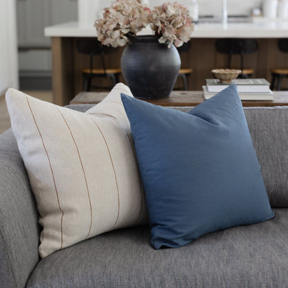 Cream striped and navy blue decorative pillows on a gray sofa.