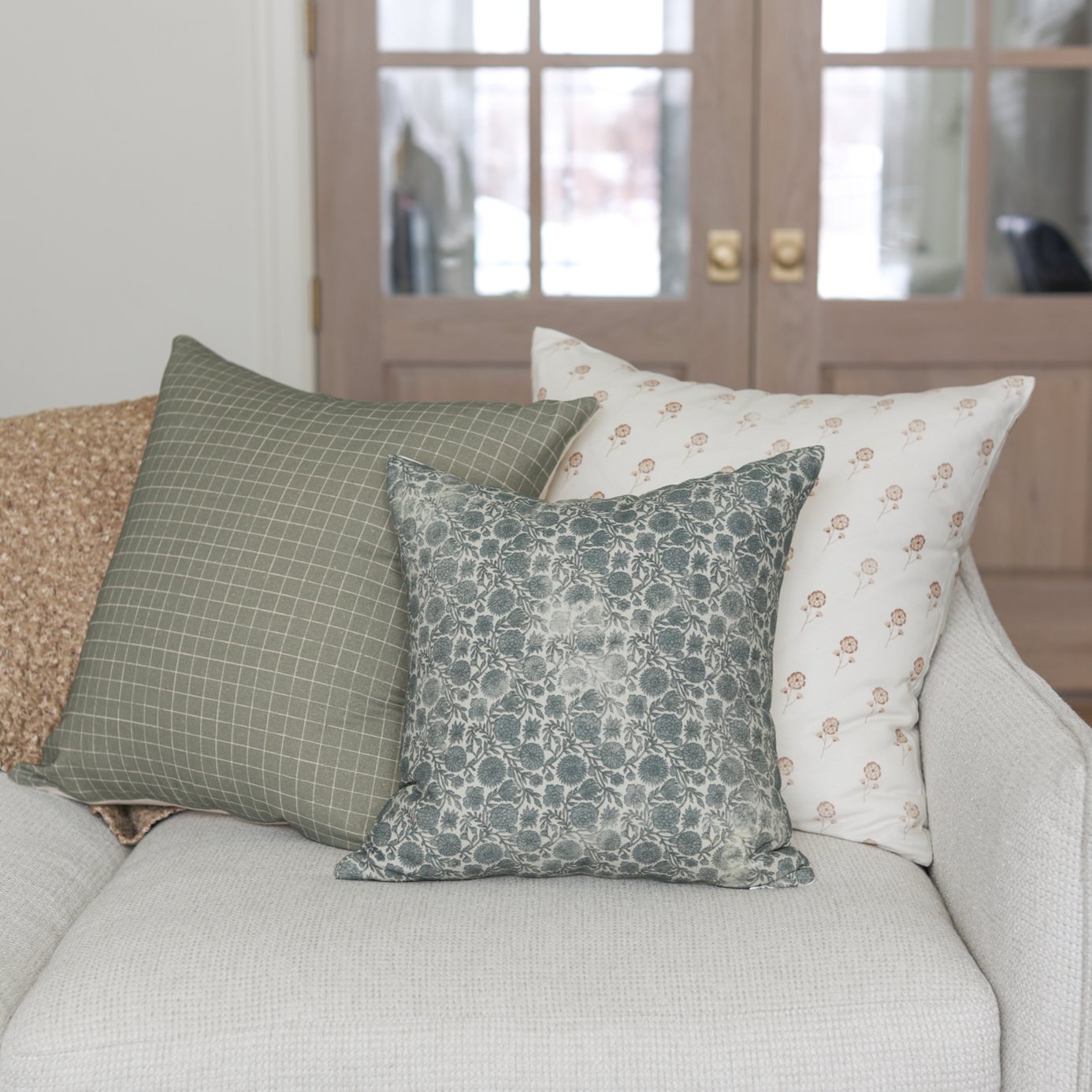 Blue floral patterned square throw pillow displayed on a cream-colored sofa with coordinating pillows.