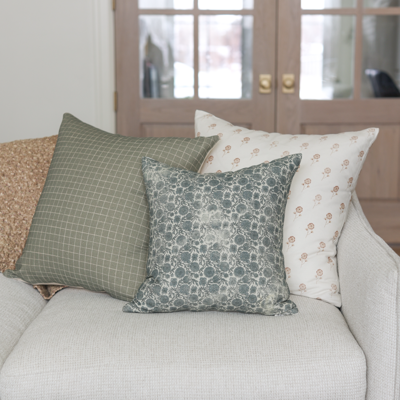 Moss green grid patterned pillow displayed on a cream sofa with coordinating pillows.