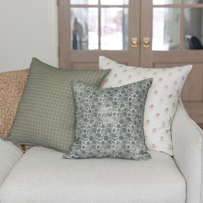 Moss green grid patterned pillow displayed on a cream sofa with coordinating pillows.