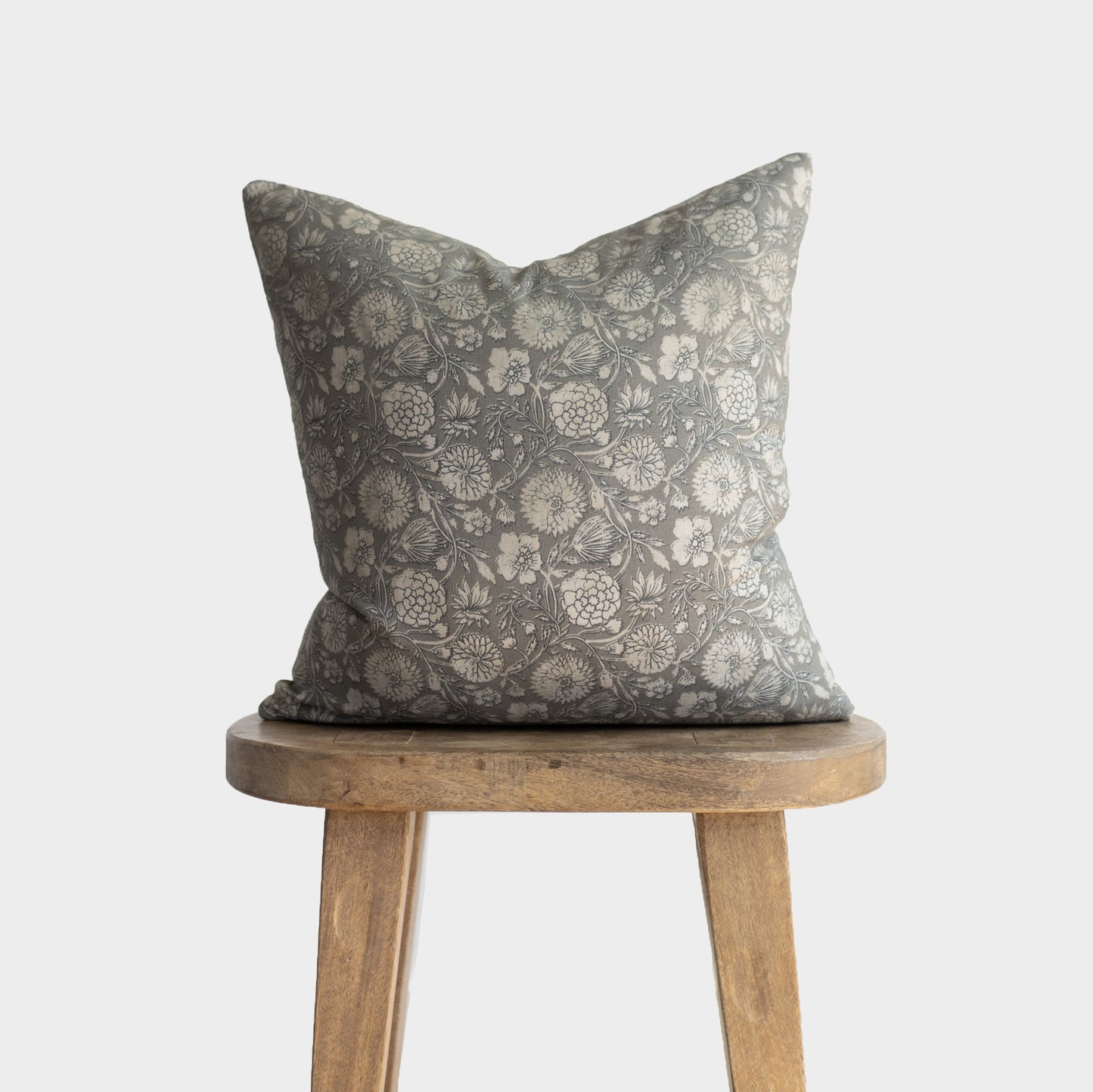 Gray and cream floral patterned throw pillow with botanical print design displayed on wooden stool.