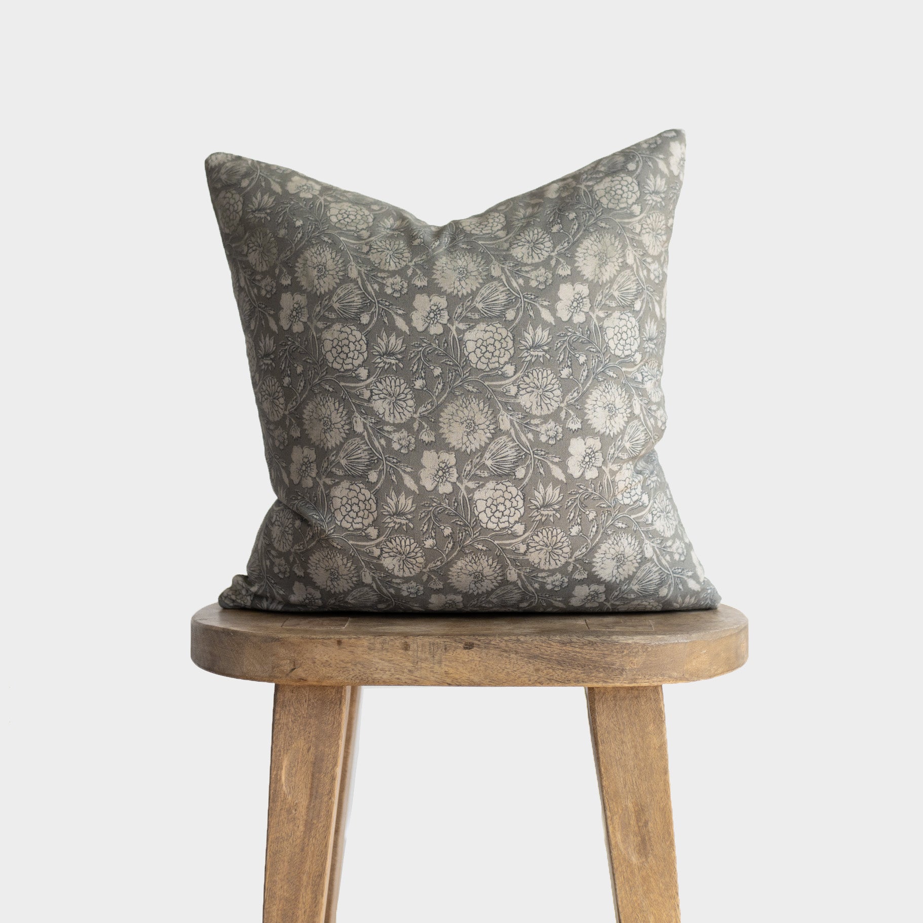 Gray and cream floral patterned throw pillow with botanical print design displayed on wooden stool.