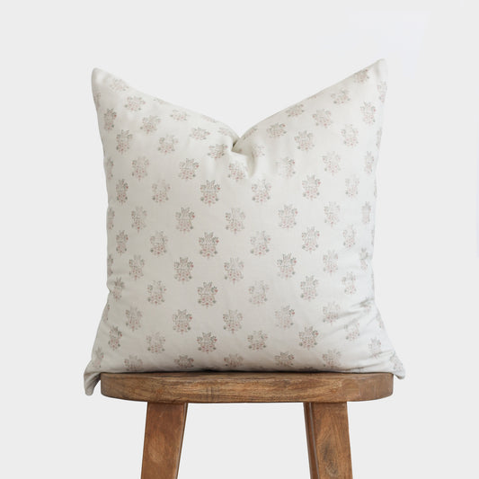 Cream pillow with small floral print in taupe and mauve tones, displayed on wooden stool.