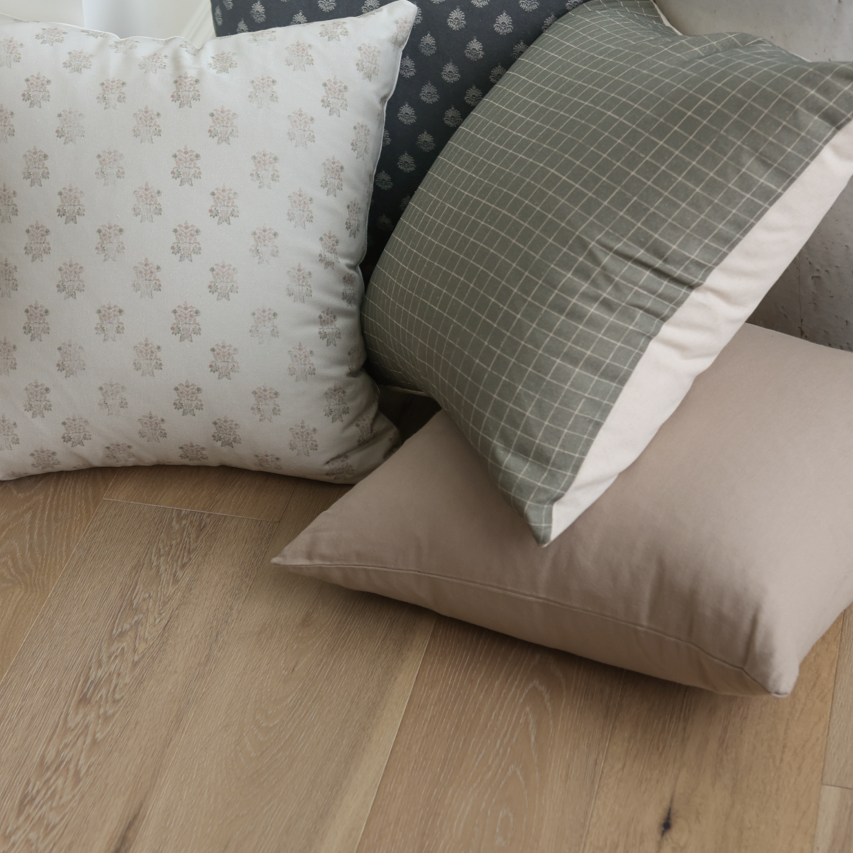 Four tan and neutral decorative pillows in varying patterns displayed on wood flooring.