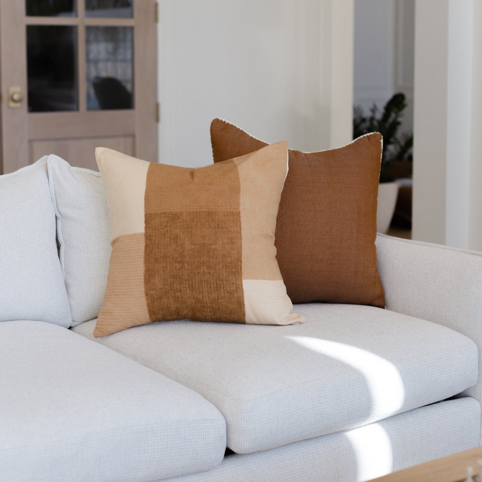 Tan and cream colorblock pillow with vertical stripe detail displayed on light gray sofa.