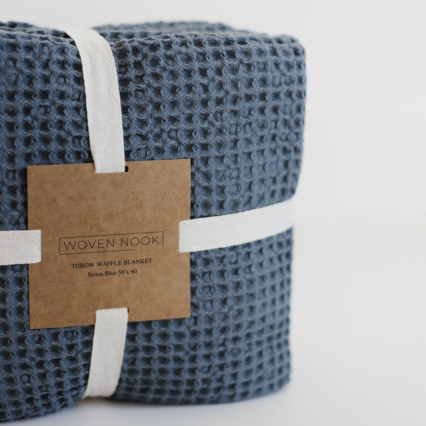 Storm blue waffle-textured throw blanket rolled and bound with white fabric straps and kraft paper label.