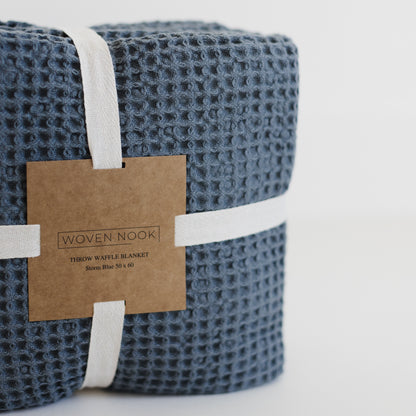 Storm blue waffle-textured throw blanket rolled and bound with white fabric straps and kraft paper label.