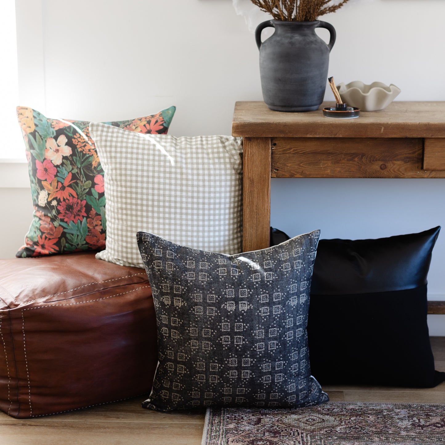 Black pillow with geometric diamond pattern displayed on floor next to floral and checkered pillows.