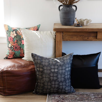 Black pillow with geometric diamond pattern displayed on floor next to floral and checkered pillows.