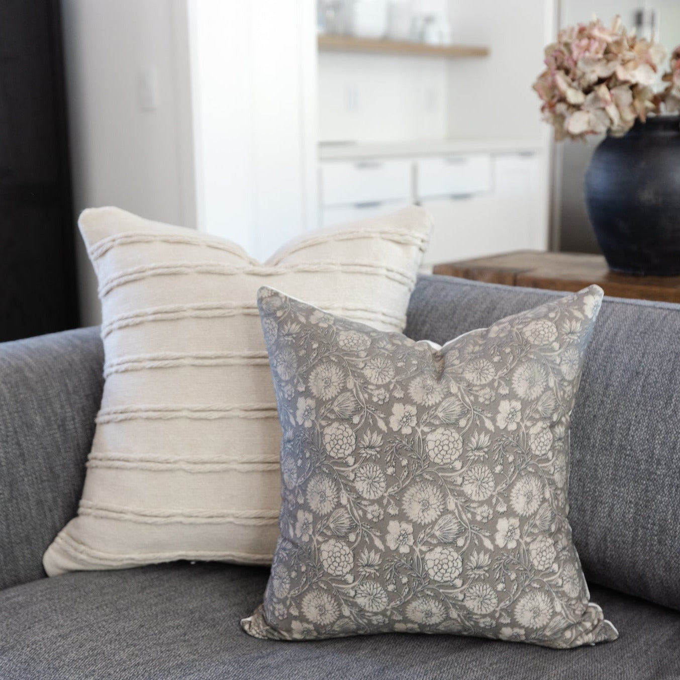 Cream striped pillow and gray floral pillow arranged on a gray upholstered sofa.