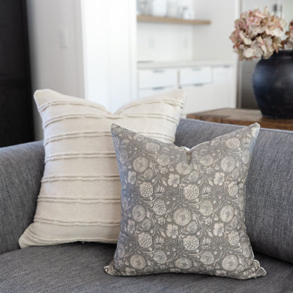 Cream striped pillow and gray floral pillow arranged on a gray upholstered sofa.