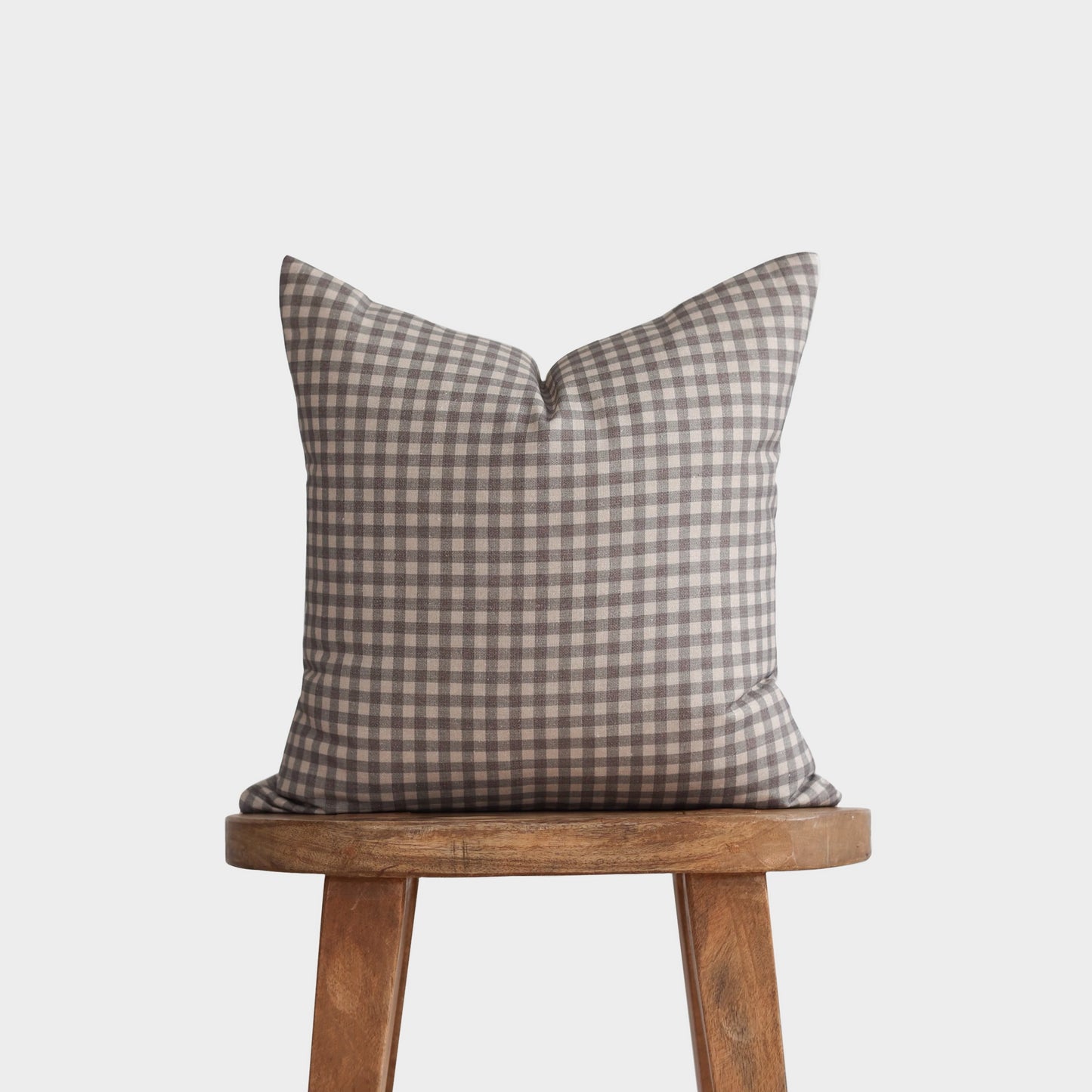 Brown and cream gingham pillow displayed on a wooden stool.