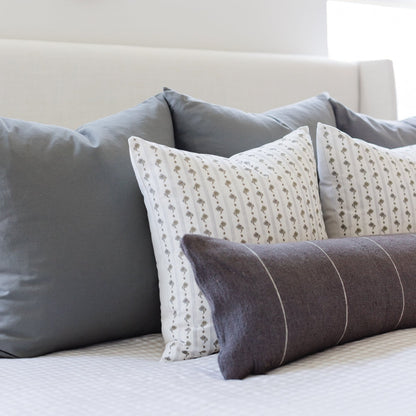 Assorted throw pillows in gray, cream with geometric print, and charcoal with stripe details arranged on a bed.