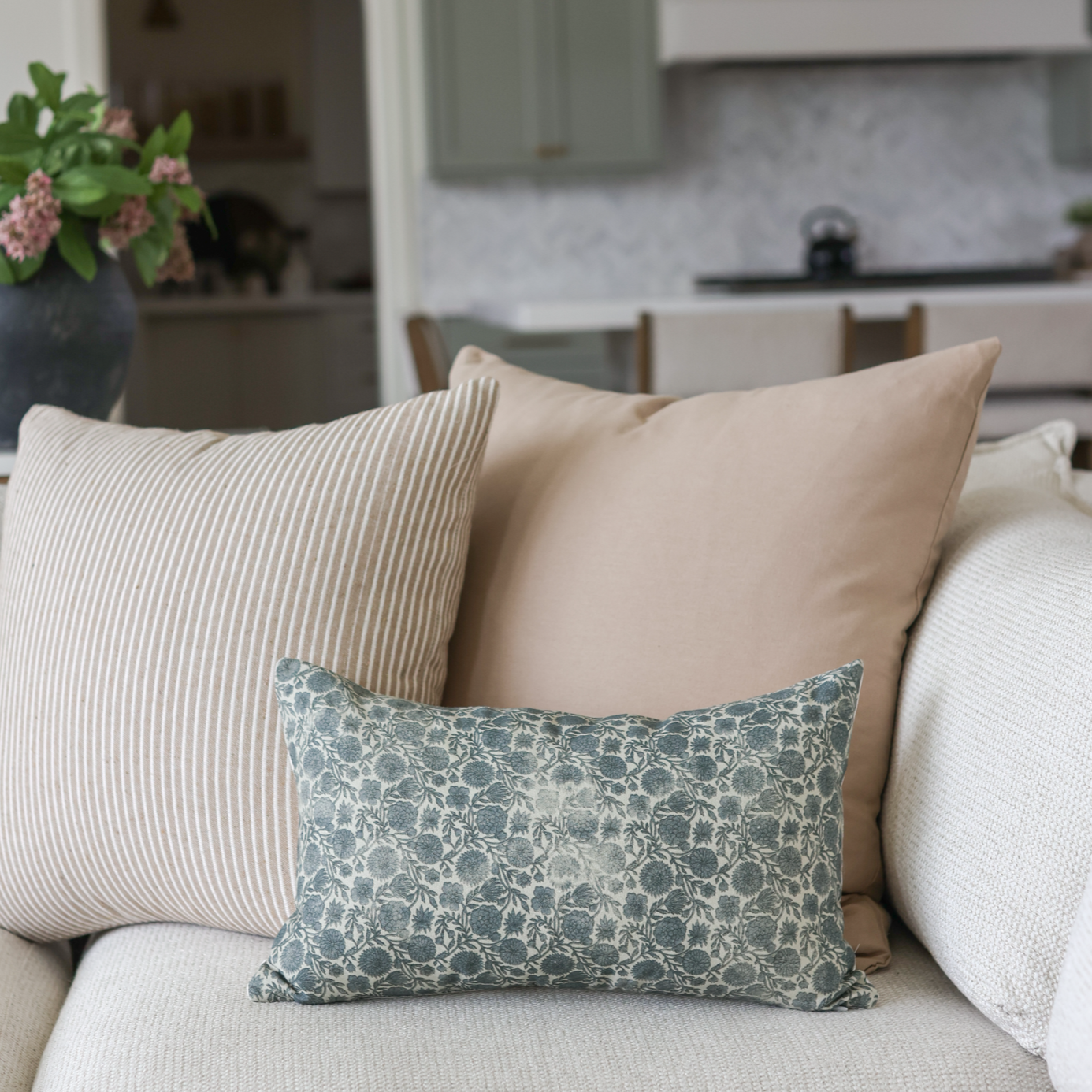 Tan solid pillow displayed with striped and patterned pillows on a beige sofa.
