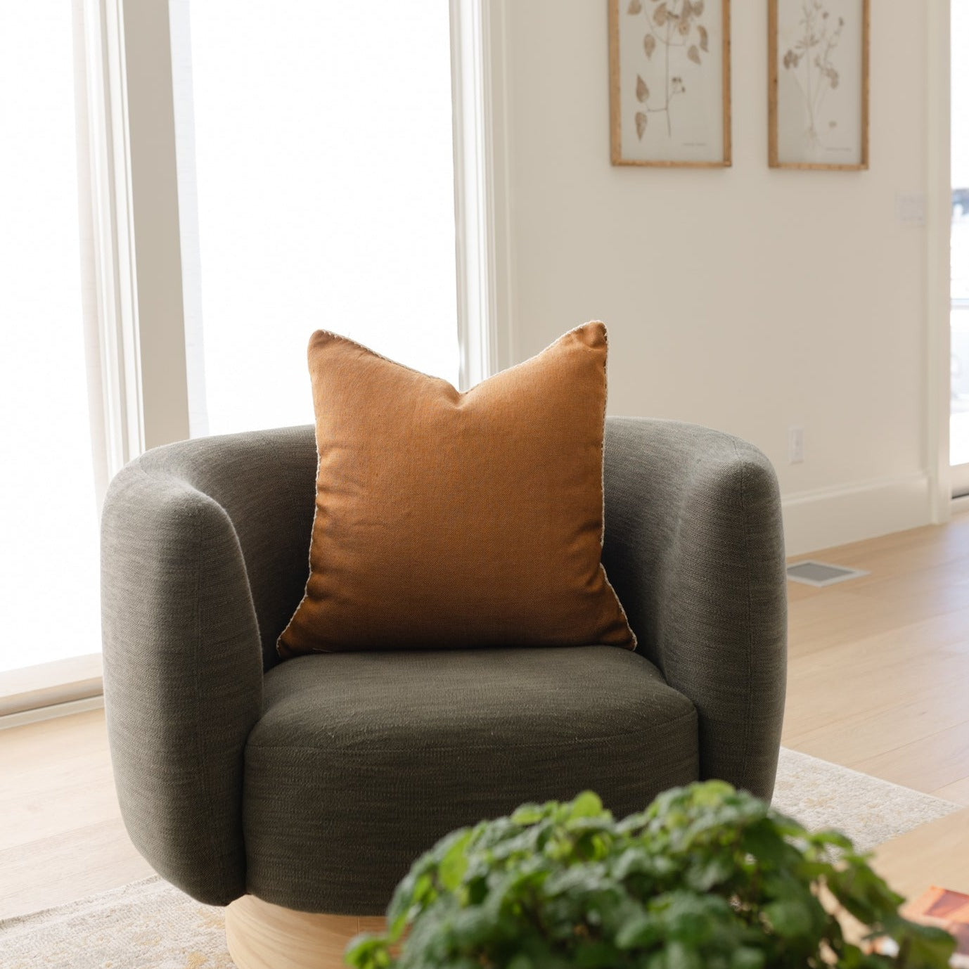 Spice-colored pillow with envelope closure on gray upholstered chair by bright window.