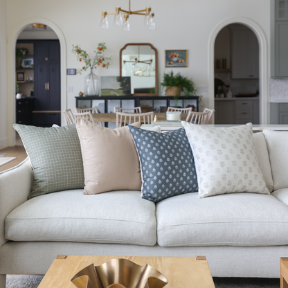 Four decorative pillows in varying patterns displayed on a cream sofa, featuring green grid, solid beige, blue geometric, and