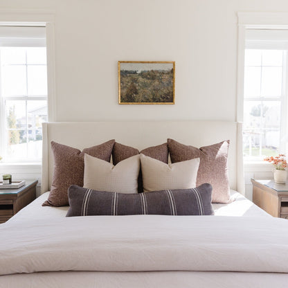 Warm charcoal lumbar pillow with textured weave displayed among coordinating pillows on a bed headboard.