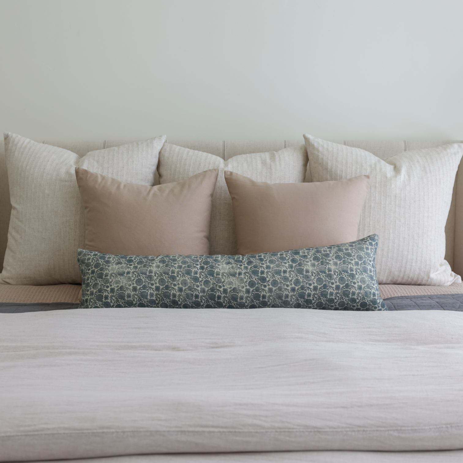 Blue patterned lumbar pillow displayed on a bed with neutral-toned pillows.