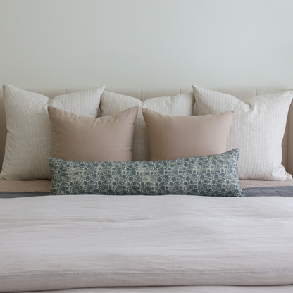 Blue patterned lumbar pillow displayed on a bed with neutral-toned pillows.