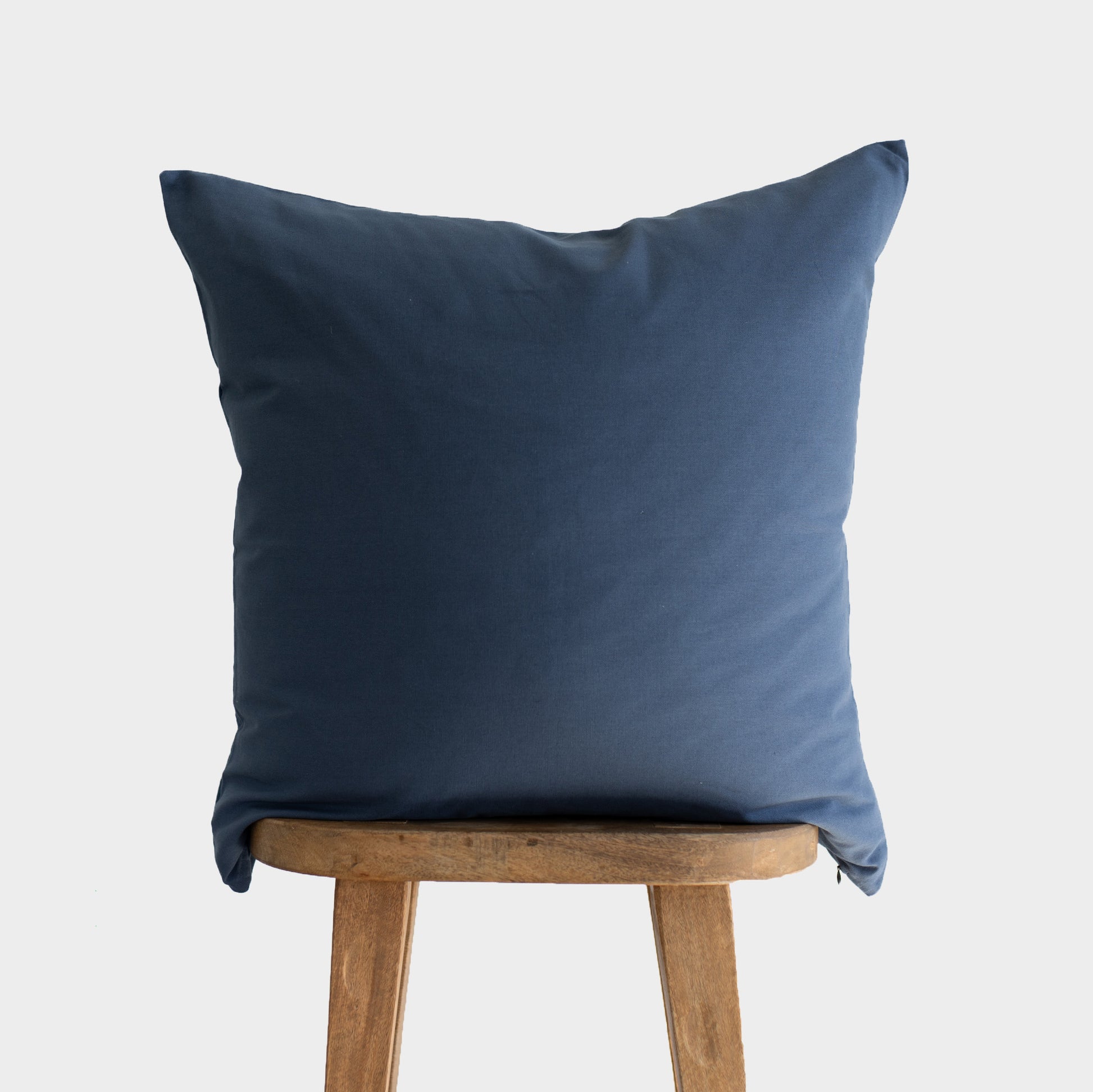 Navy blue square pillow with knife edge seams displayed on a wooden stool.