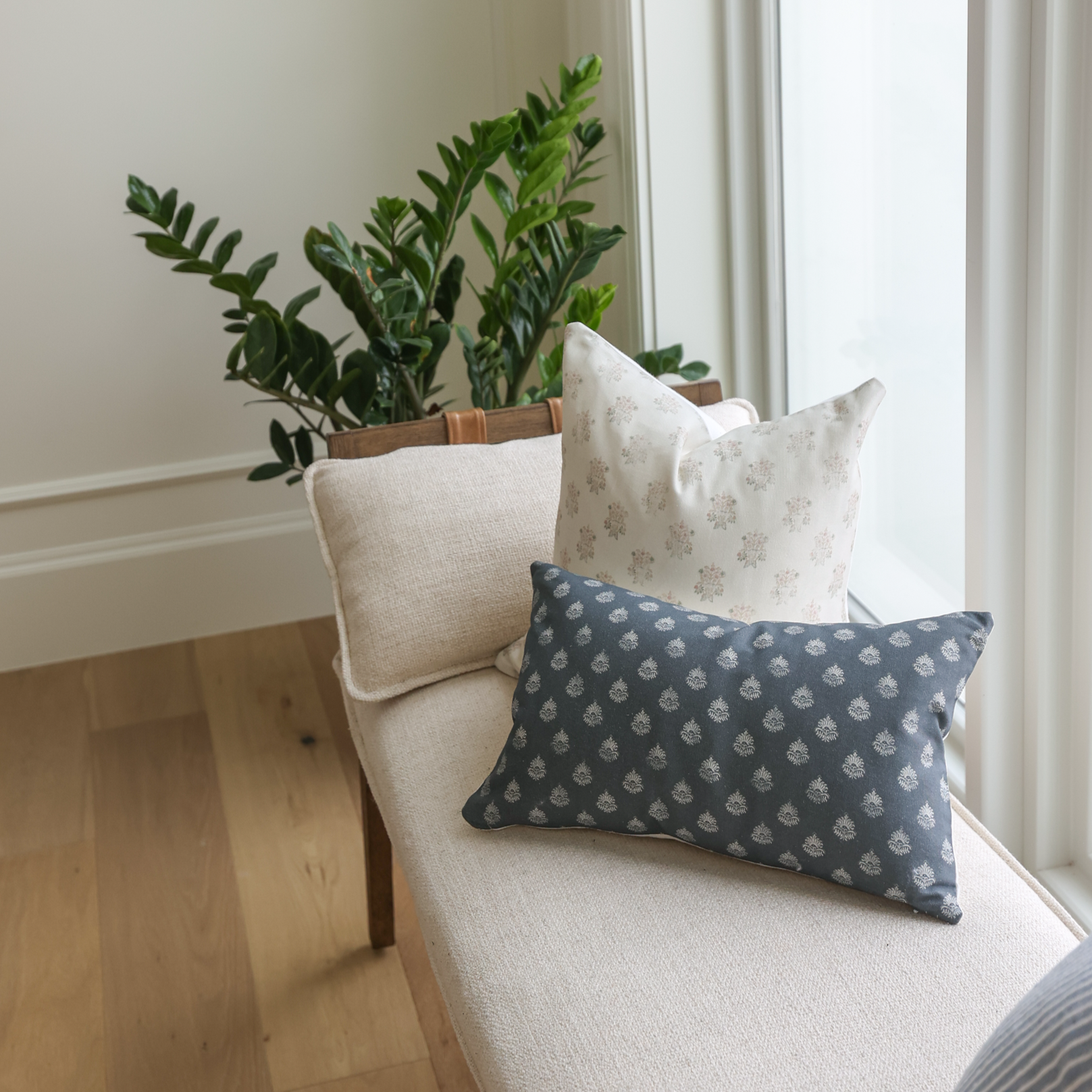 Dark blue lumbar pillow with small repeating leaf pattern, displayed on cream chair with other pillows.