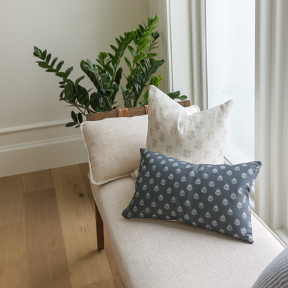 Dark blue lumbar pillow with small repeating leaf pattern, displayed on cream chair with other pillows.