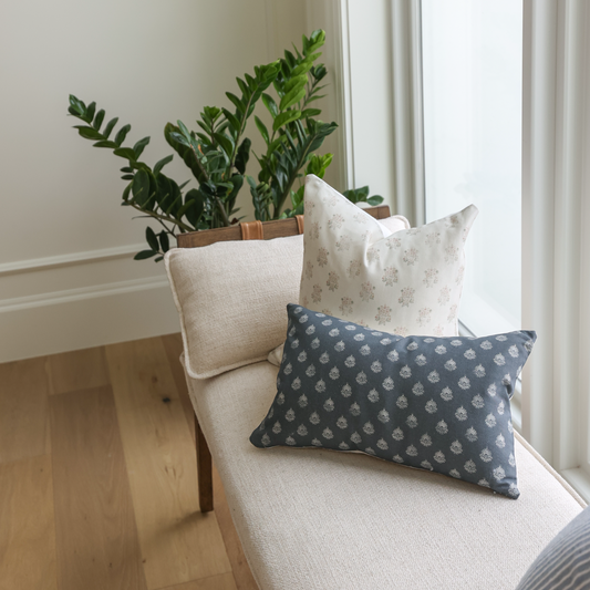 Dark blue lumbar pillow with small repeating leaf pattern, displayed on cream chair with other pillows.