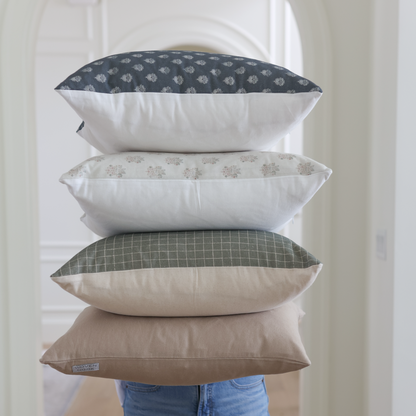 Four stacked throw pillows in navy patterned, beige patterned, green grid, and solid tan fabrics.