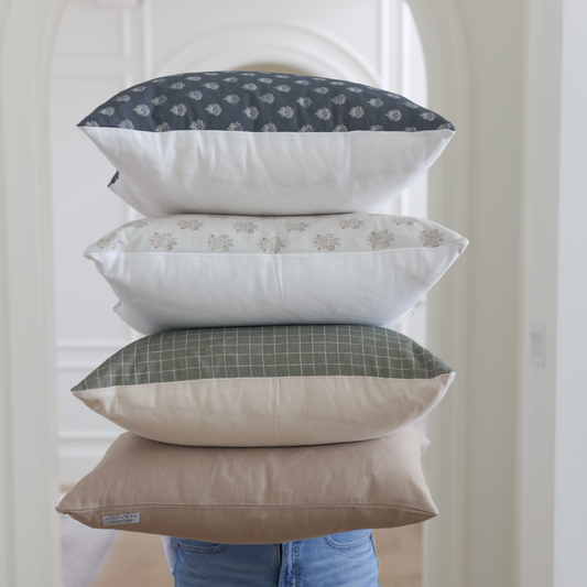 Four stacked throw pillows in navy patterned, beige patterned, green grid, and solid tan fabrics.