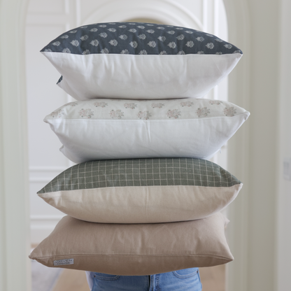 Stack of four decorative pillows in navy, cream, sage green, and tan with various patterns displayed against white door.
