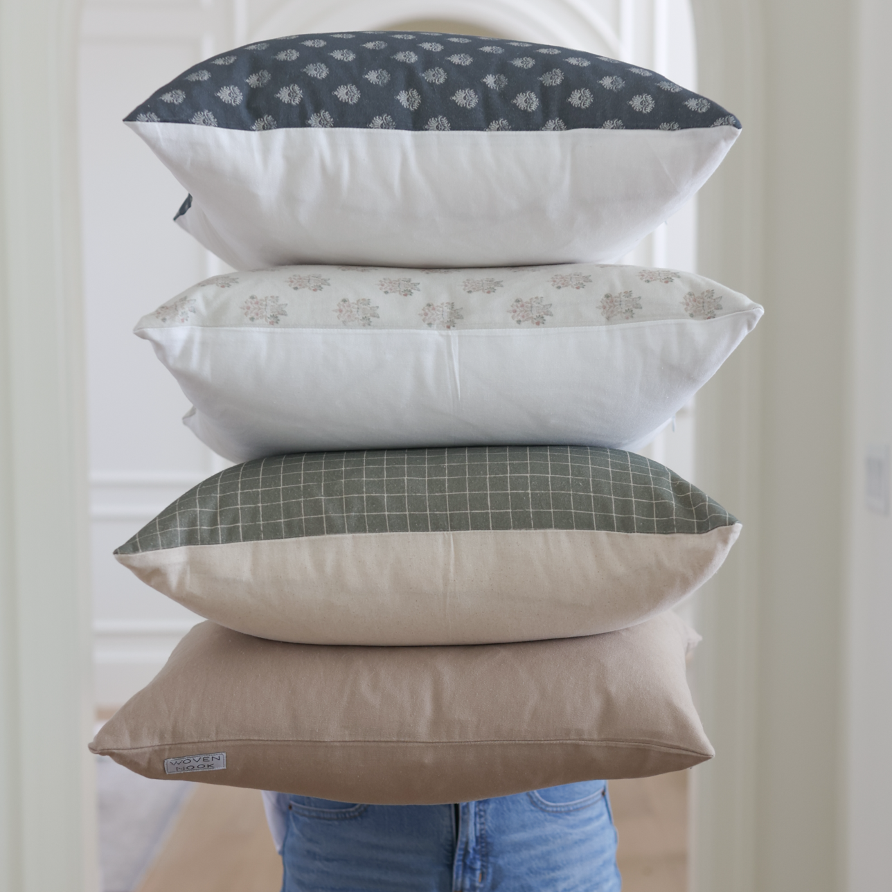 Stack of four pillows with moss green grid pattern on bottom pillow, solid sides in cream and white, and patterned tops in da