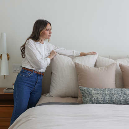Blue patterned lumbar pillow displayed on a bed with neutral bedding and decorative pillows.