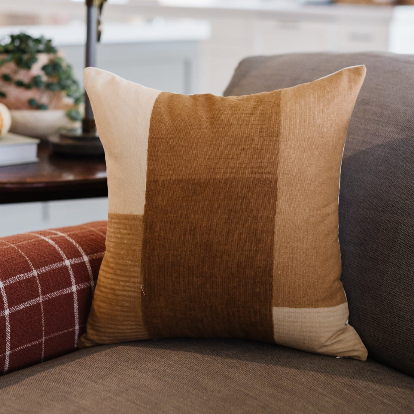 Tan and brown color-block pillow with textured fabric panels displayed on gray sofa.