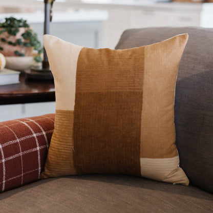 Tan and brown color-block pillow with textured fabric panels displayed on gray sofa.